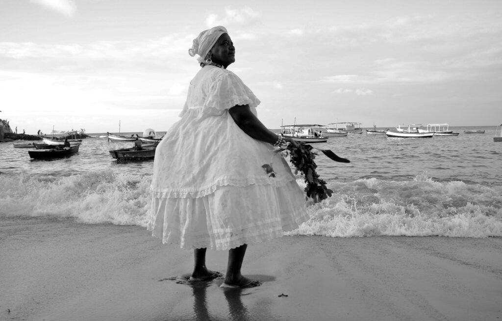 Image of a 'Baiana', in traditional clothing, by the sea.